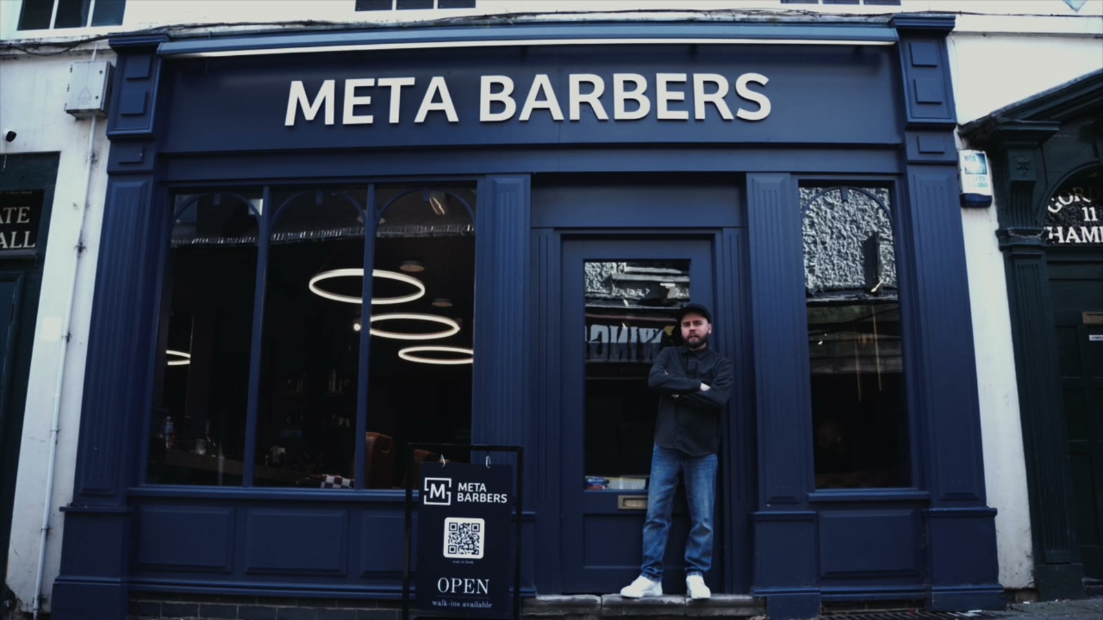 The Meta Barbers shopfront: a dark blue frontage with the name above the window and a barber standing in the doorway
