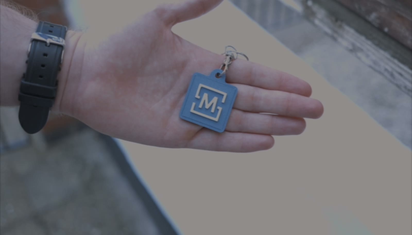 A 3D-printed key ring with an M logo resting in an open palm